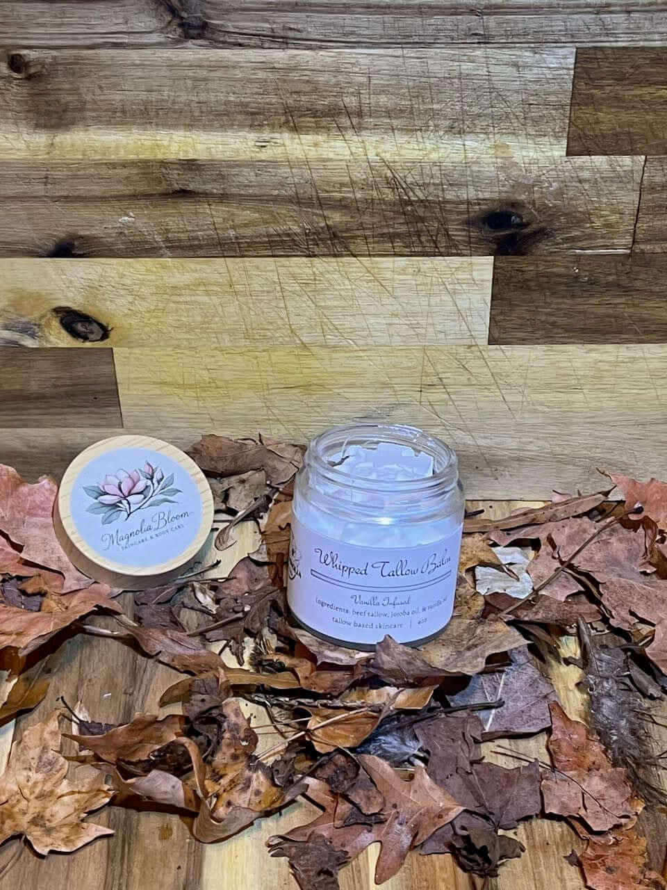 Whipped Tallow Balm with Vanilla jar displayed among autumn leaves on a wooden surface.